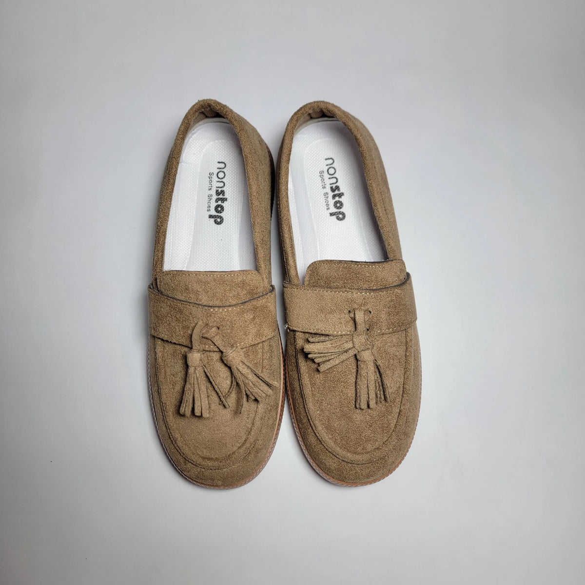 A pair of tan suede tassel loafers with white insoles, displayed on a light gray background.