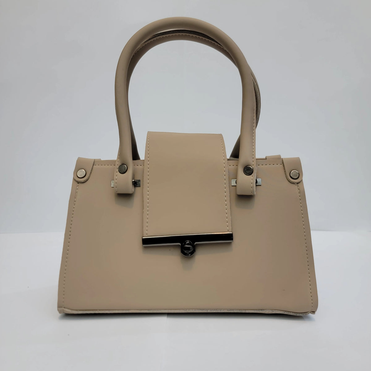 A structured beige faux-leather handbag with dual top handles, a front flap detail, and silver-tone hardware, photographed against a neutral light gray background.