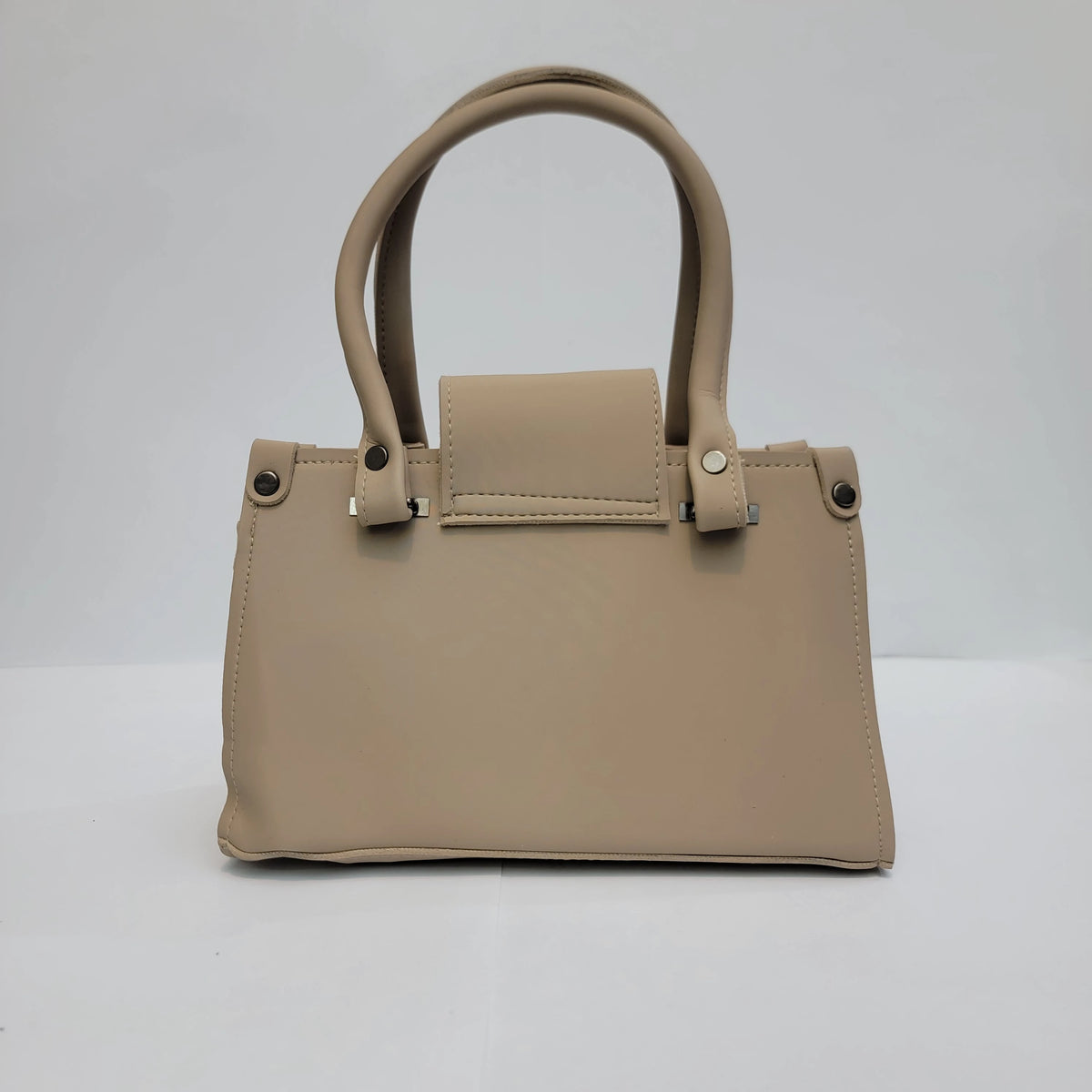 A structured beige faux-leather handbag with double top handles, a front flap detail, and silver-tone hardware, photographed against a neutral light gray background.