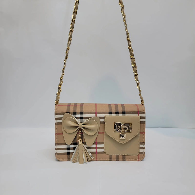 A beige plaid shoulder bag with a large beige bow and tassel charm on the front, a flap pocket with a gold-tone turn-lock clasp, and a gold-tone chain strap, shown against a plain light gray background.