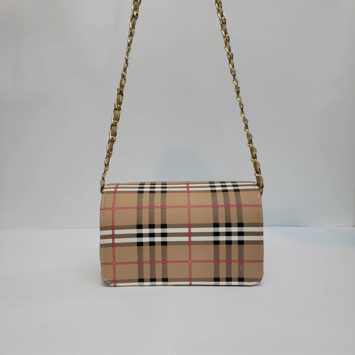 A small shoulder bag with a beige plaid pattern featuring black, white, and pink stripes, complete with a gold chain strap, set against a plain light gray background.