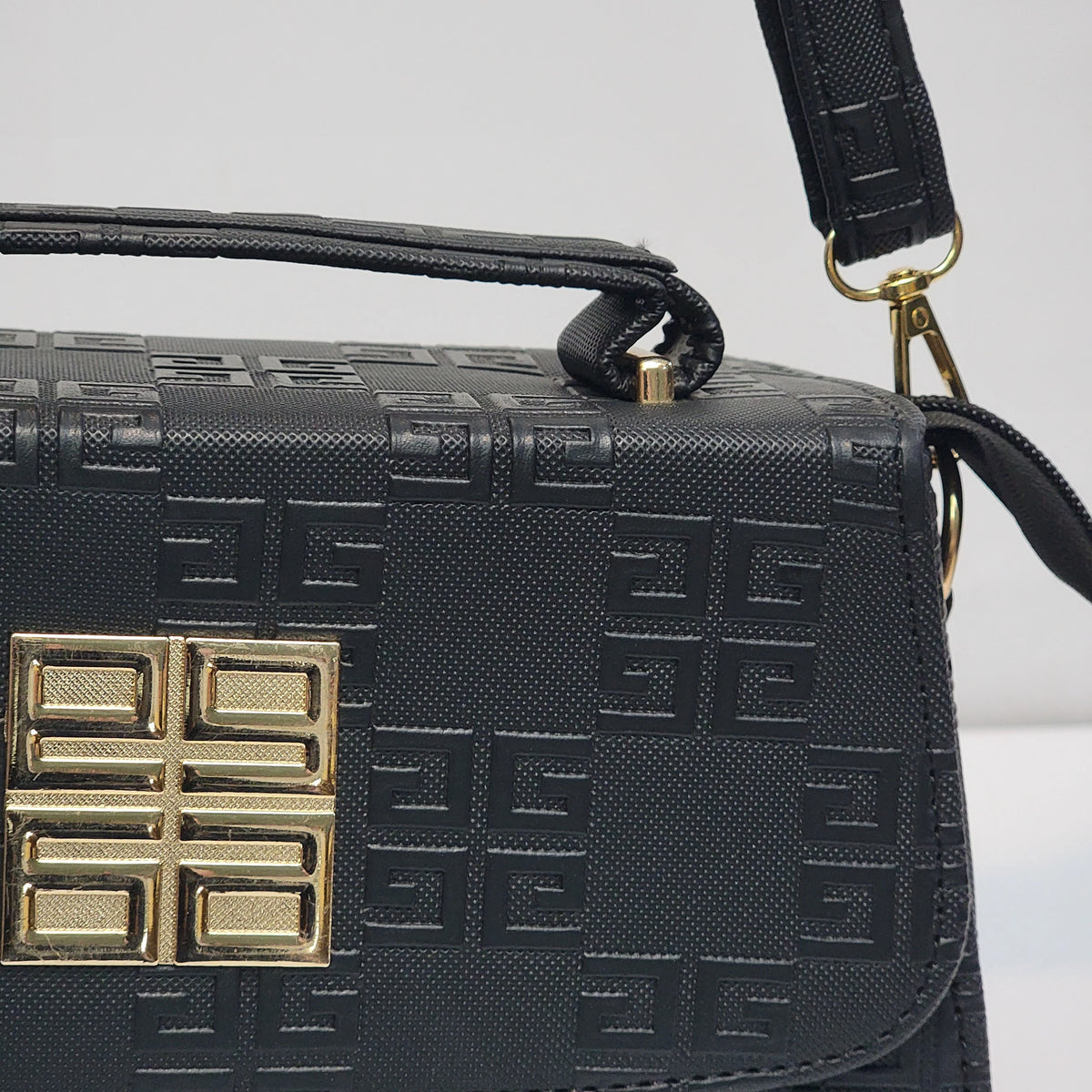 A close-up of a black Givenchy handbag featuring the brand's signature embossed Greek key pattern and a gold-tone front logo clasp.