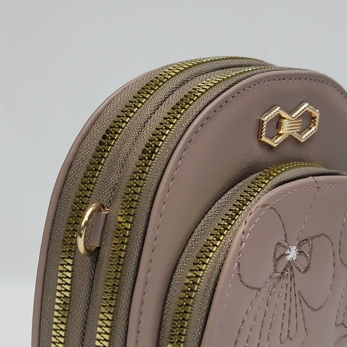 Close-up of a taupe leather zippered pouch with gold-tone hardware, including a bow-shaped zipper pull and a matching embroidered bow detail on the front pocket.