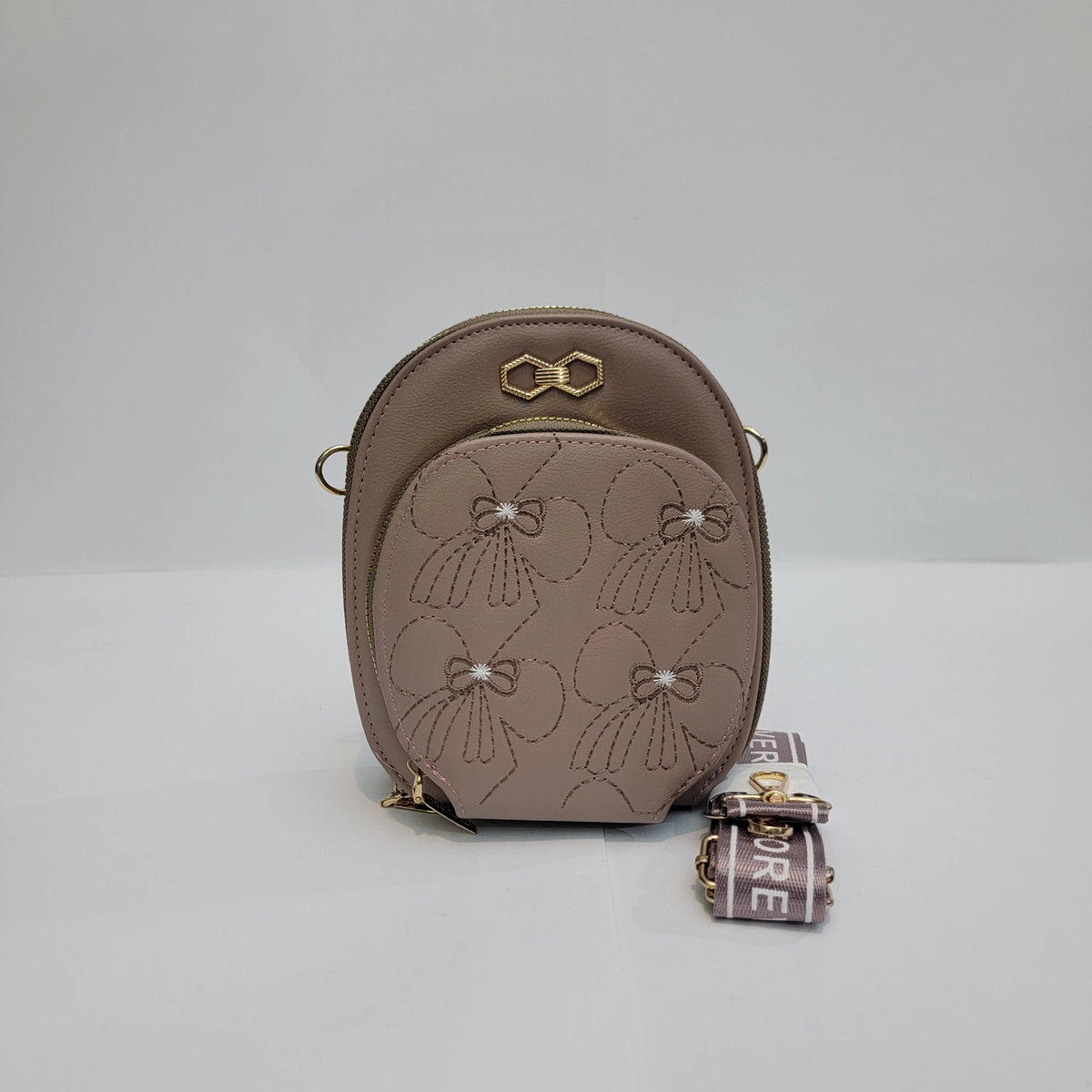A small taupe leather crossbody bag with a front pocket featuring stitched floral motifs and pearl-like accents, gold-tone hardware, and a matching printed strap.