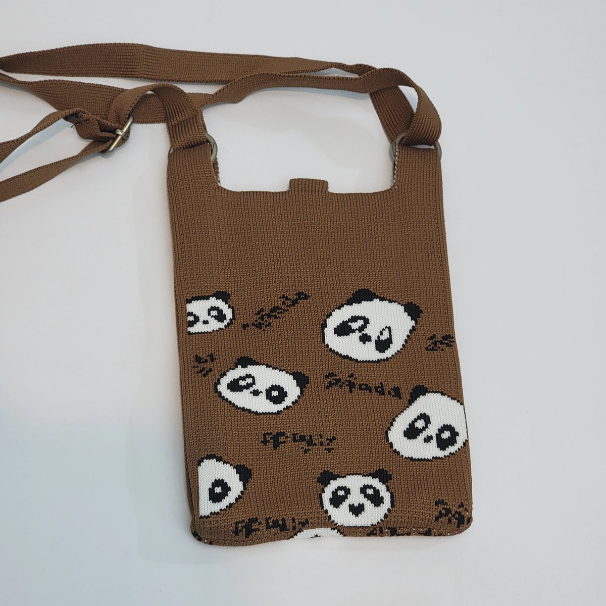 A brown knitted phone pouch with a repeating panda face pattern, featuring a matching adjustable shoulder strap, photographed on a light gray background.