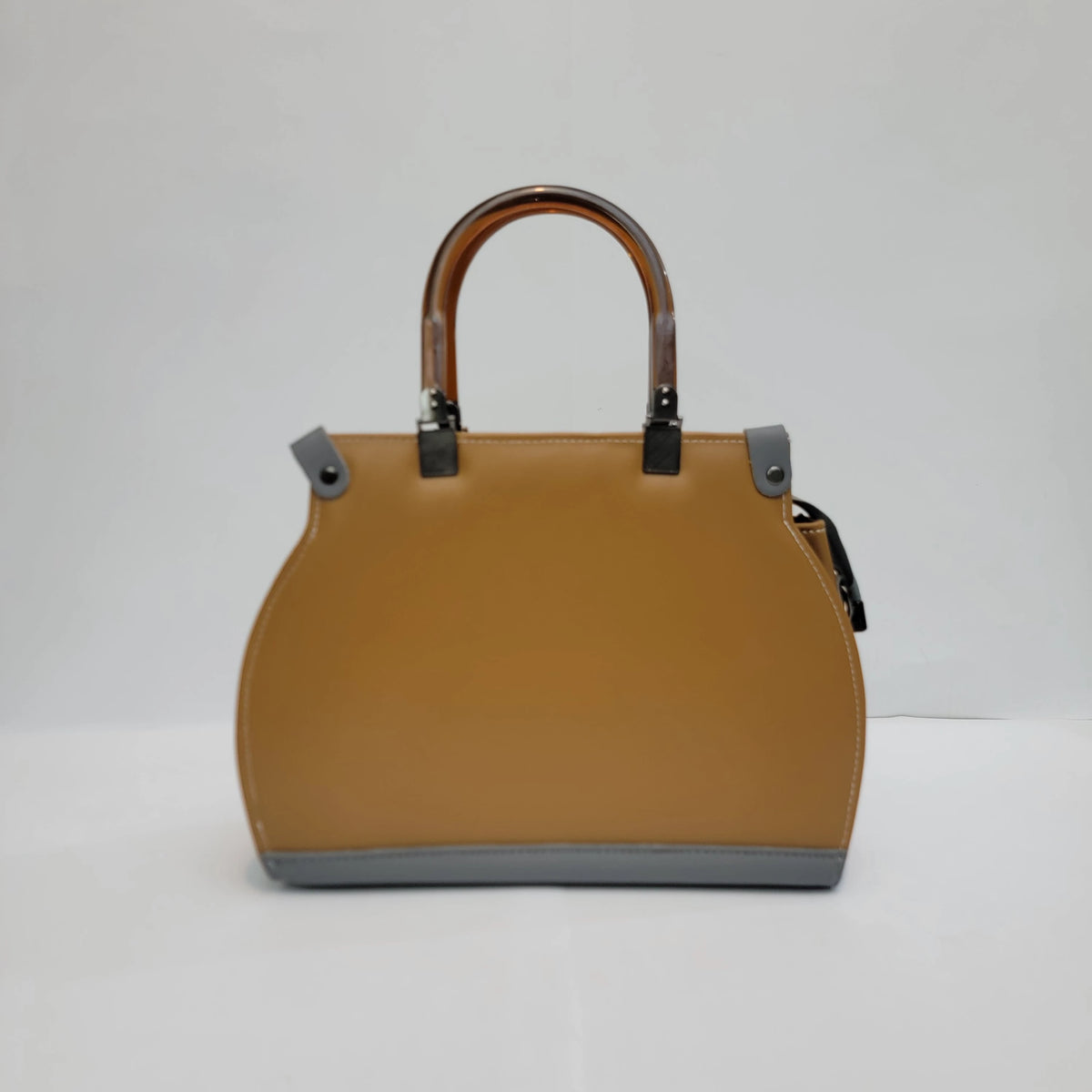 A structured tan leather handbag with a curved top handle, gray accents on the base and side tabs, and dark metal hardware, photographed against a plain light gray background.