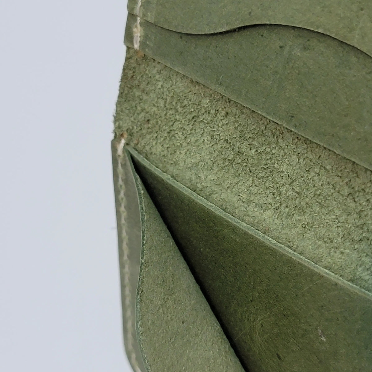 An olive green leather card holder wallet, close-up of stitching detail