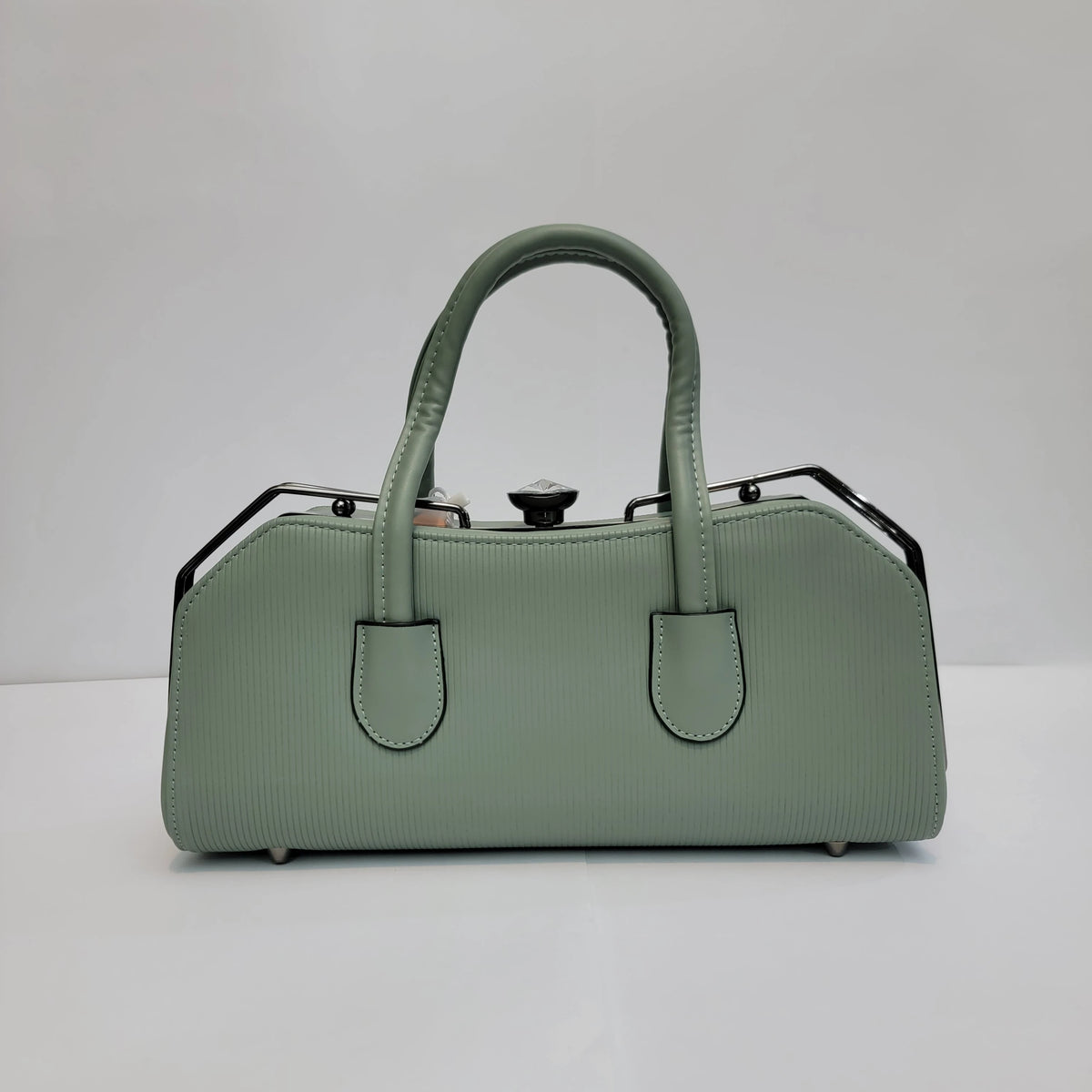 A sage green textured leather handbag with double top handles and black metal side accents, photographed against a plain light gray background.