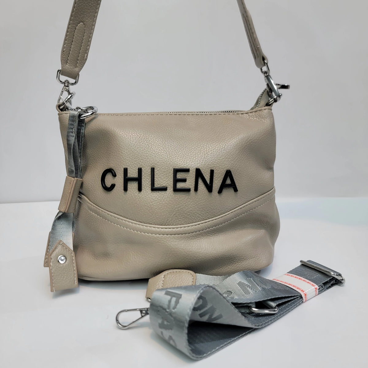 A beige pebbled leather shoulder bag with 'CHLENA' embroidered in black across the front, shown with a matching gray patterned detachable strap on a white background.