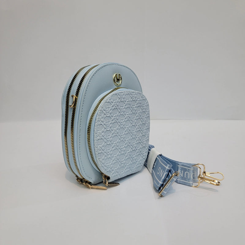 A light blue faux-leather mini backpack with a front embossed pattern pocket, dual gold-tone zippers, and a matching blue and white patterned detachable shoulder strap with gold hardware.