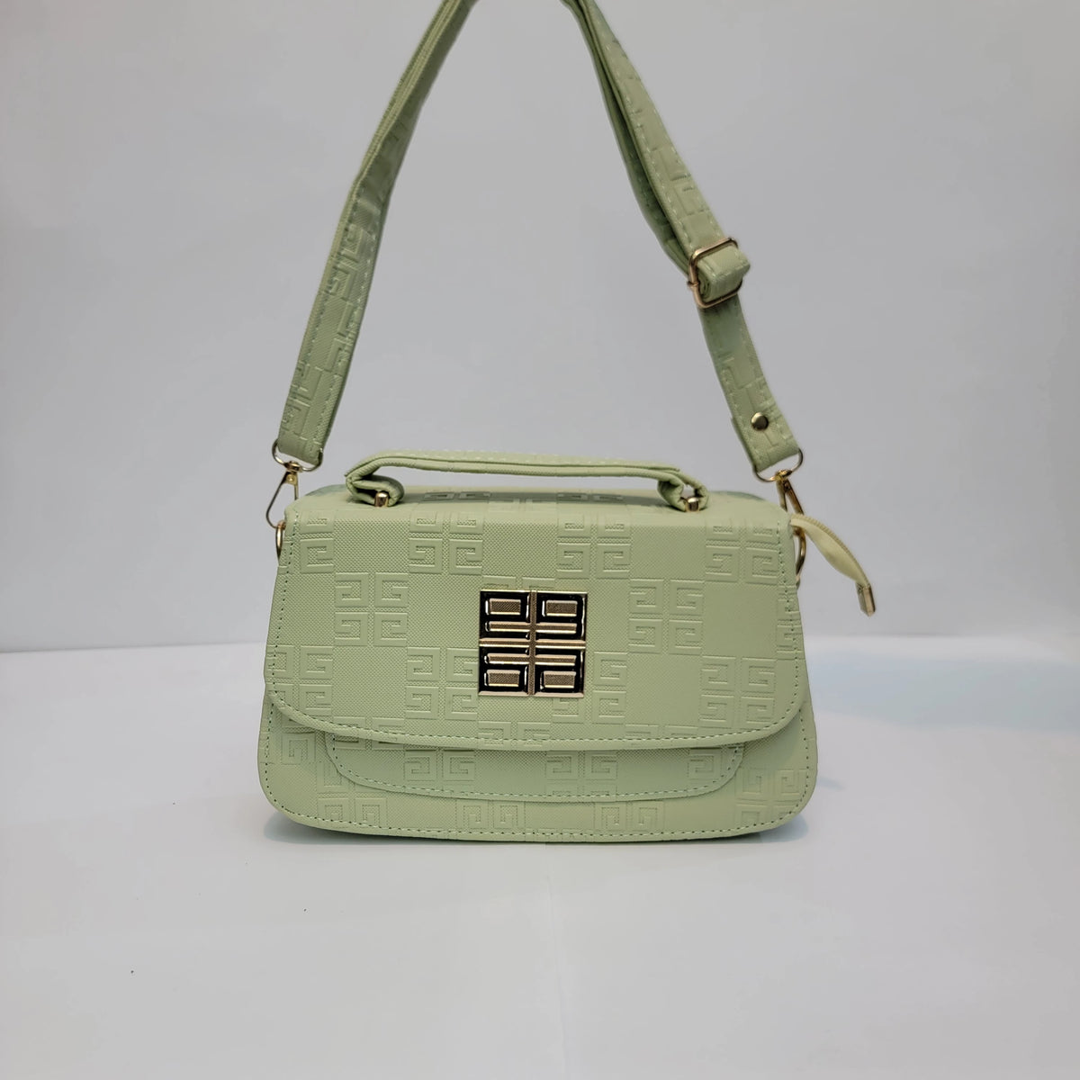 A light sage green embossed leather handbag with a top handle, adjustable shoulder strap, and a gold-toned four-ring logo clasp on the front flap.