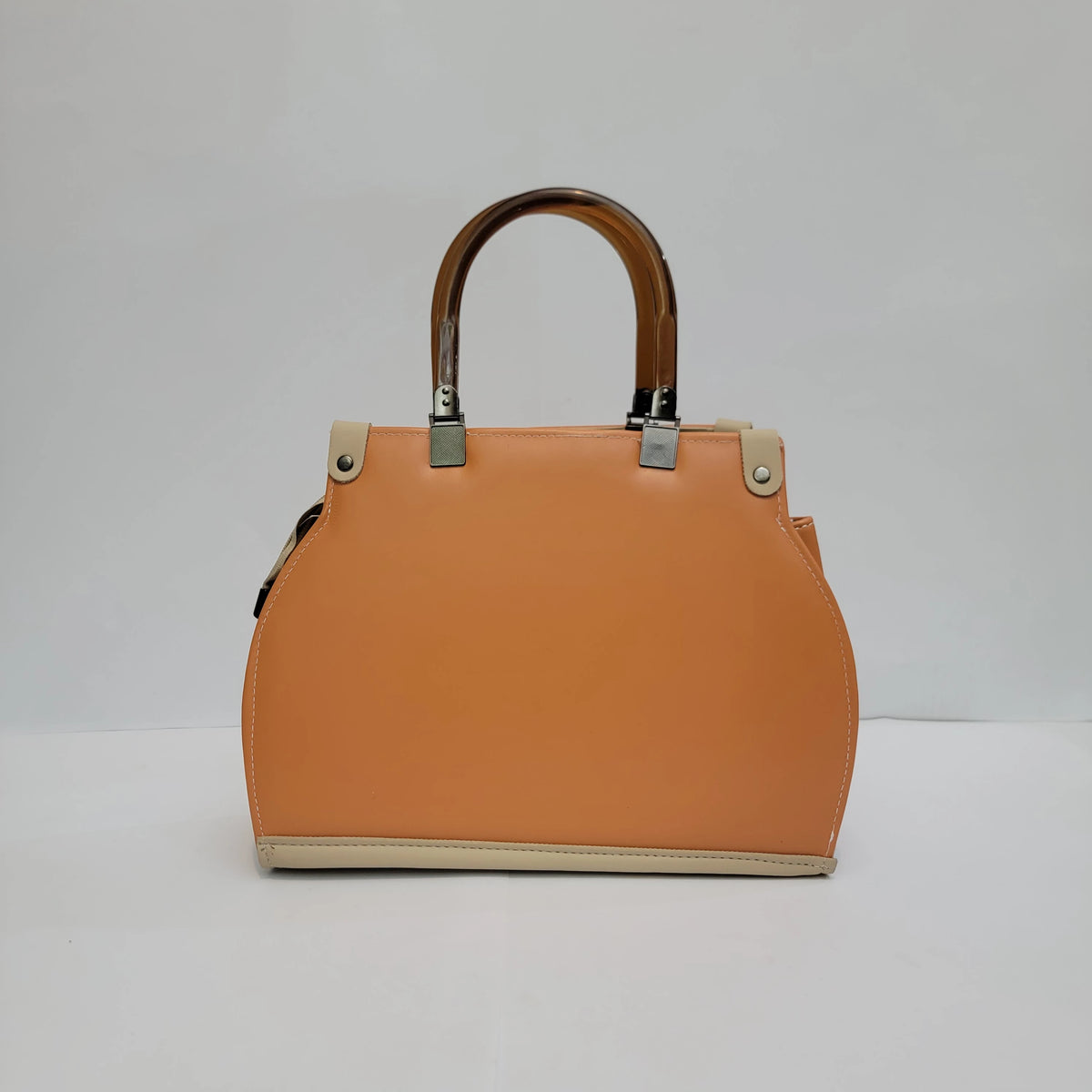 A structured leather handbag in a warm peach-orange color, featuring dark brown top handles, silver-tone hardware, and a beige leather trim at the base and on the handle attachments, set against a plain light gray background.
