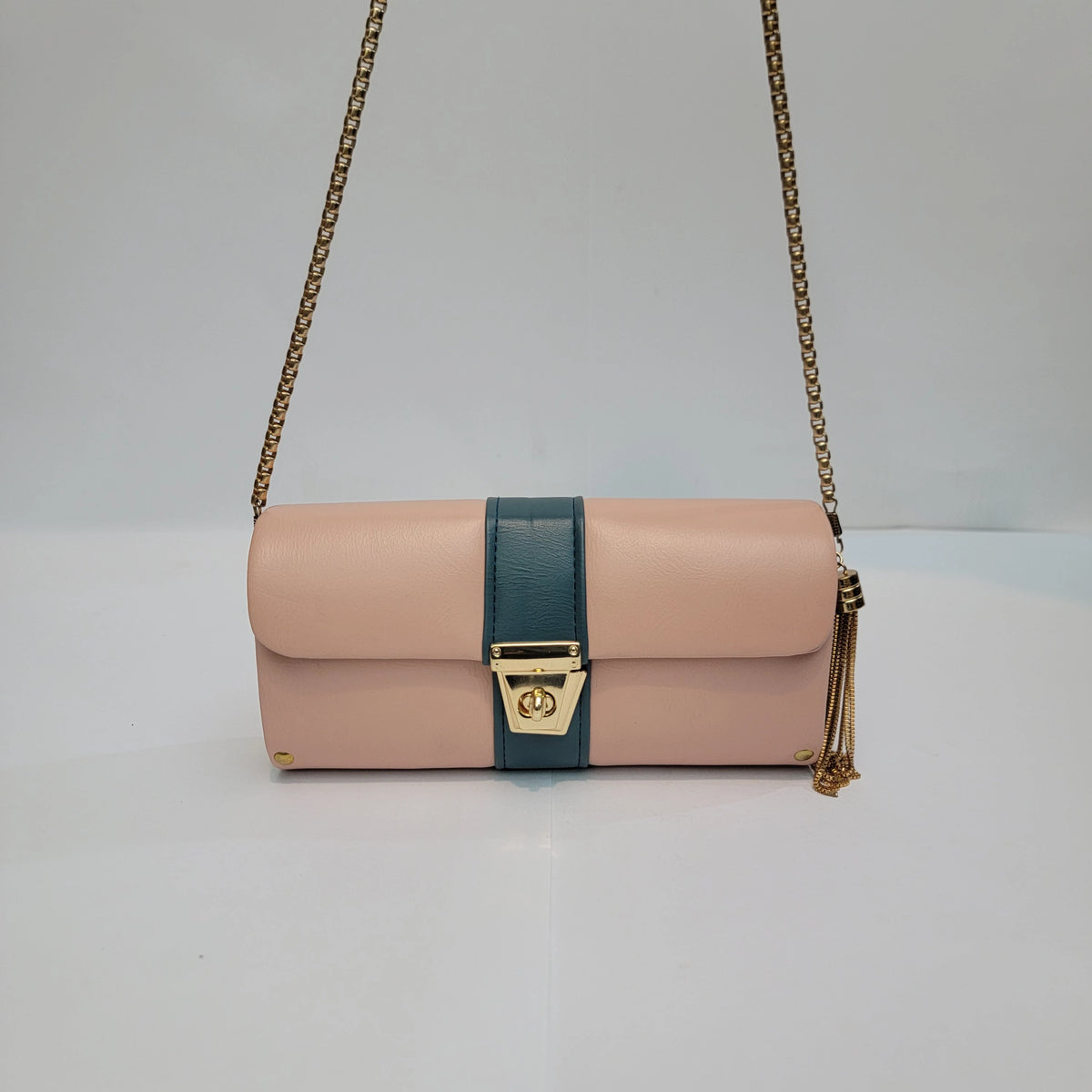 A structured shoulder bag in blush pink and teal leather with gold-tone hardware, featuring a chain strap and a tassel detail.