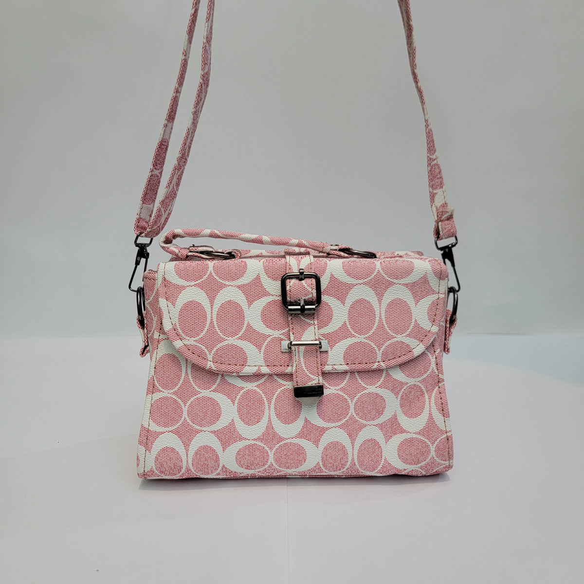 A pink and white patterned crossbody handbag with a top handle, adjustable shoulder strap, and front flap secured by a buckle, shown against a plain light gray background.
