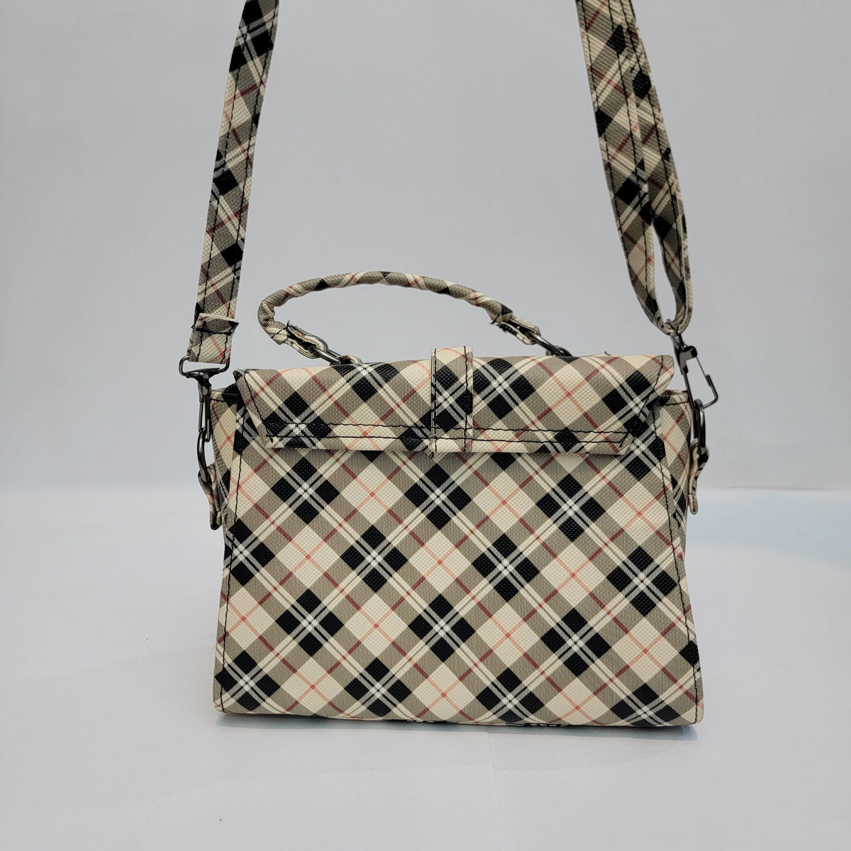 A structured handbag with a top handle and shoulder strap, featuring a beige, black, and white plaid pattern with thin red accent lines, set against a plain light gray background.