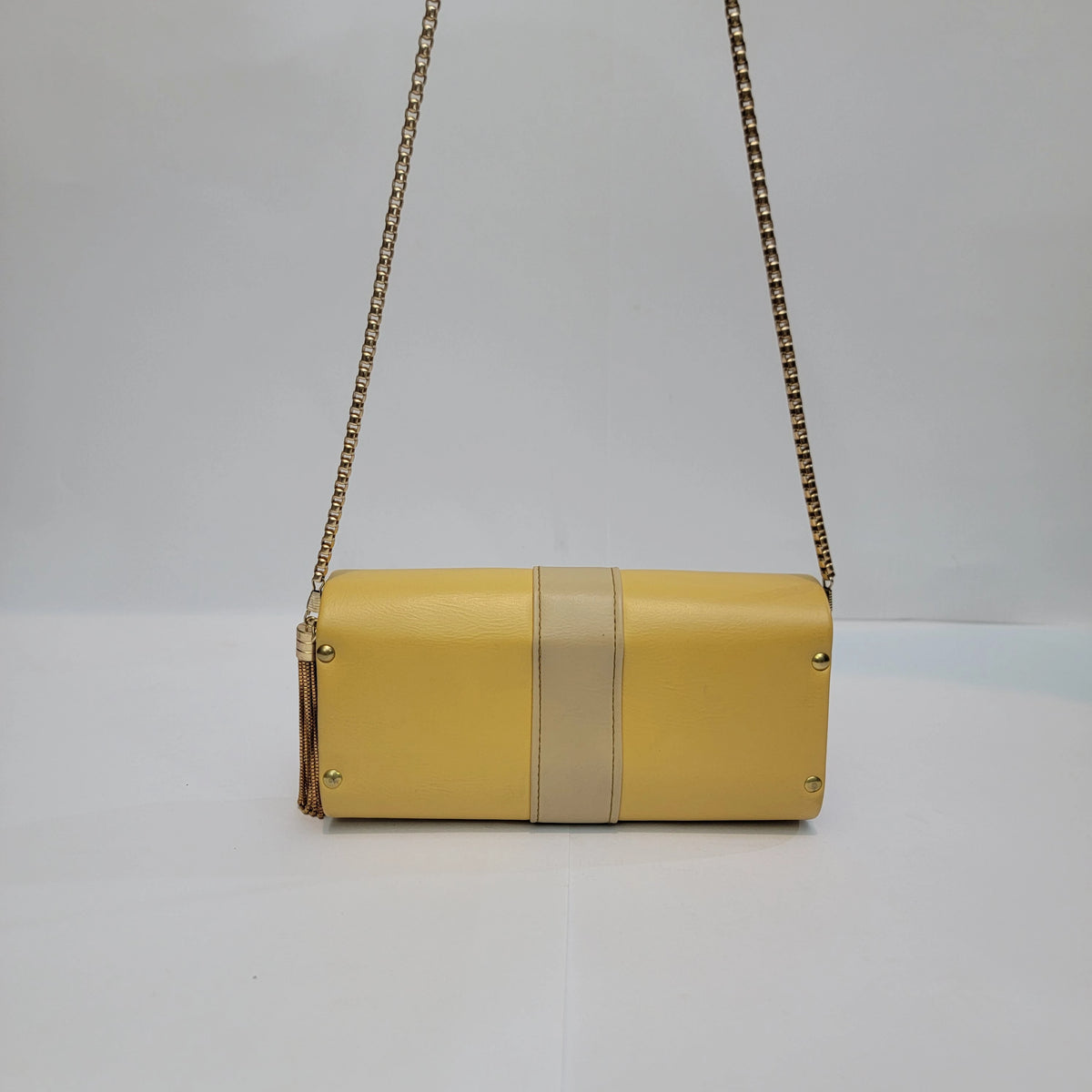 A yellow leather clutch bag with a beige center stripe and gold-tone chain strap, shown against a plain white background.